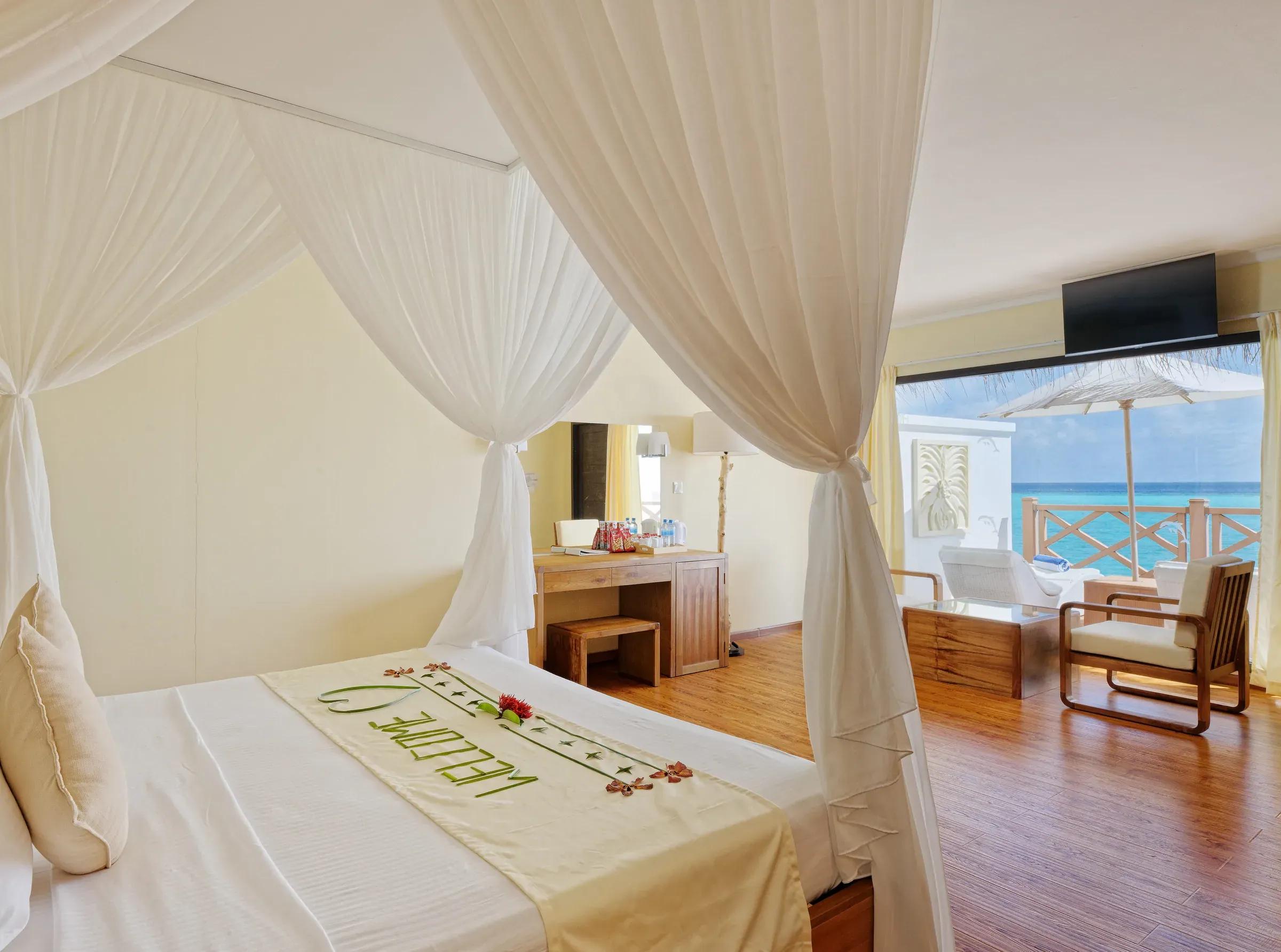 Interno del Premium Water Bungalow con letto a baldacchino e terrazza vista mare al Angaga Island Resort & Spa.
