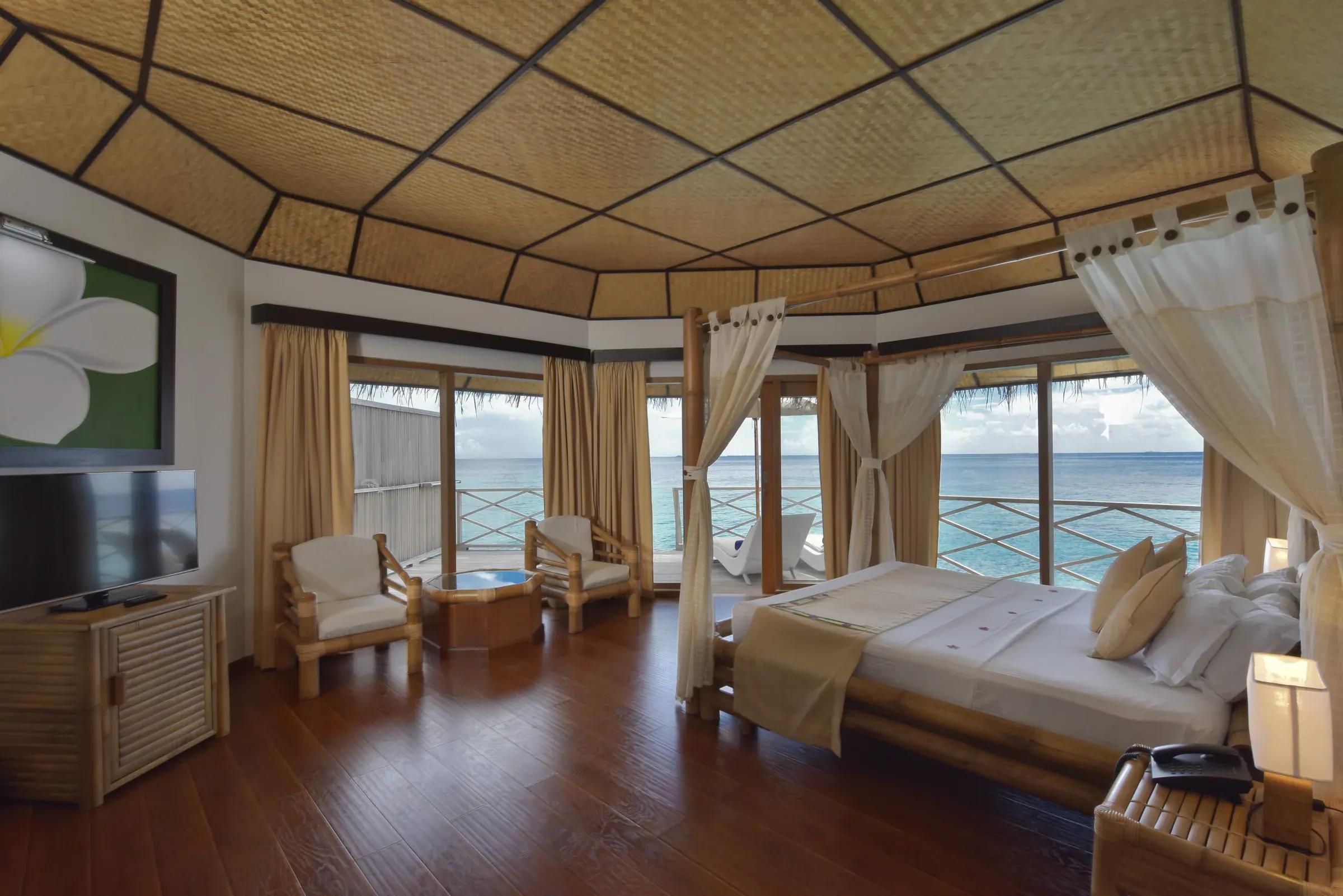 Interno del SUPERIOR WATER BUNGALOW con letto a baldacchino e vista mare al Angaga Island Resort & Spa.