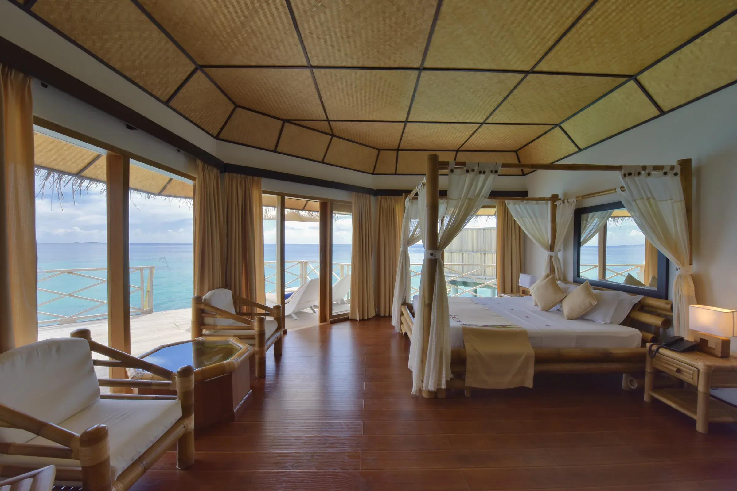 Vista interna del SUPERIOR WATER BUNGALOW con letto a baldacchino e terrazza sul mare al Angaga Island Resort & Spa.