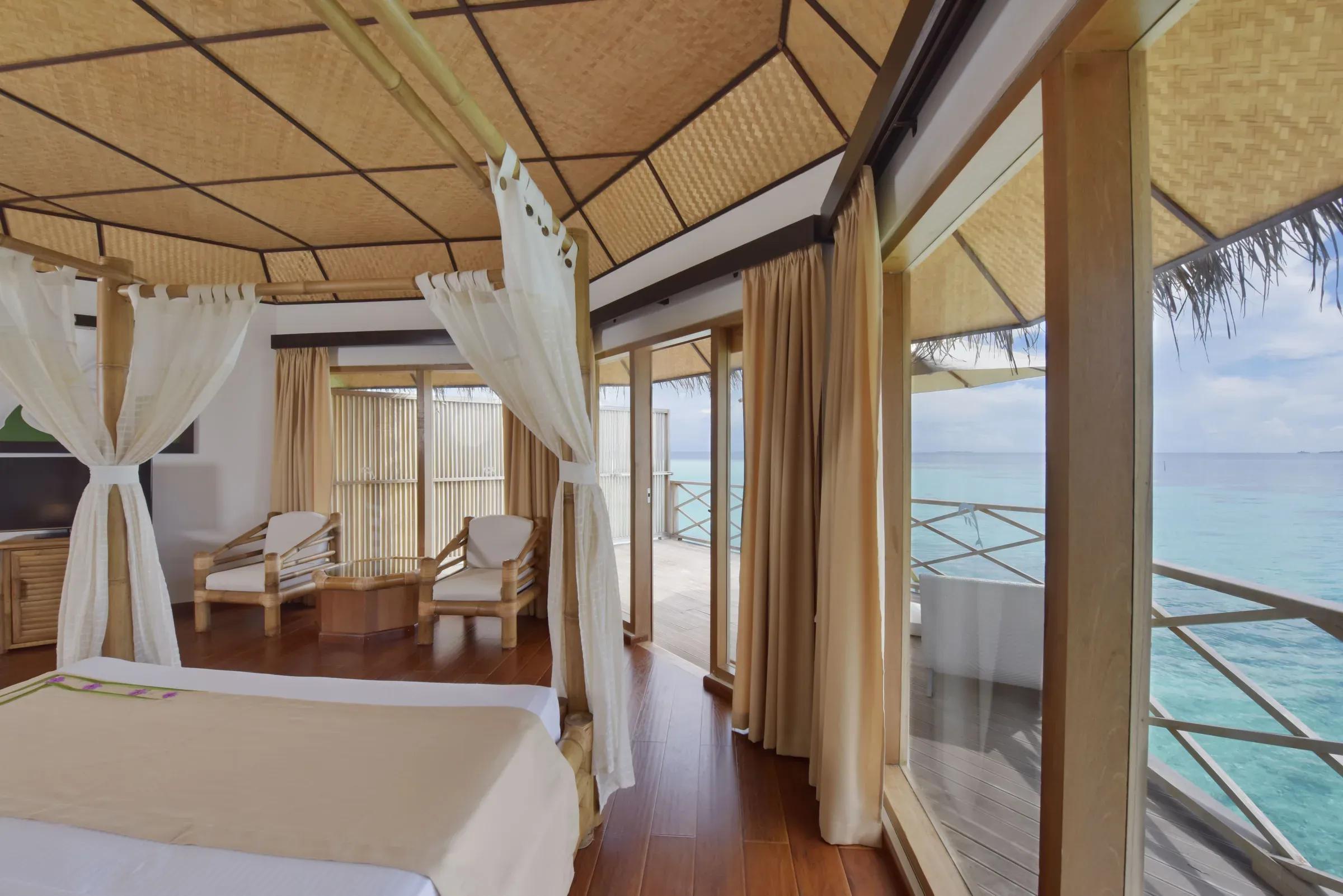 Interno del SUPERIOR WATER BUNGALOW con letto a baldacchino e vista sull'oceano al Angaga Island Resort & Spa.