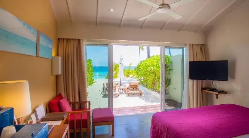 Vista dalla Lagoon View Beach Villa con letto, TV e accesso diretto alla spiaggia del Centara Ras Fushi Resort & Spa Maldives.