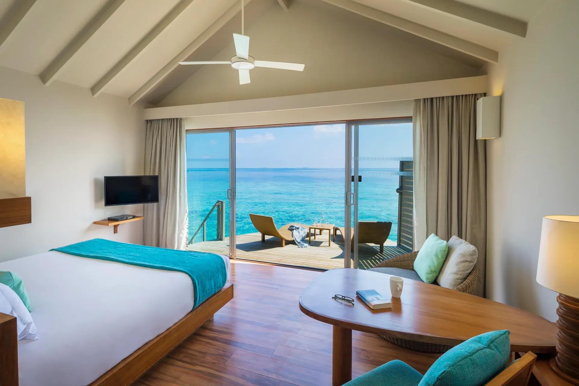 Camera da letto della Sunset Overwater Villa con vista sull'oceano e terrazza al Centara Ras Fushi Resort & Spa Maldives.