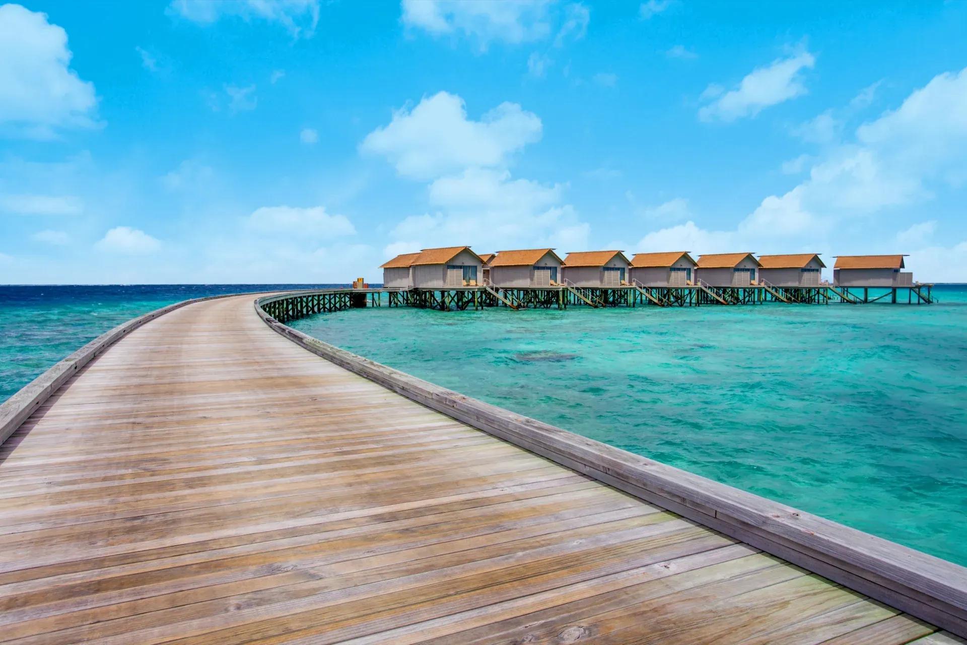 Passerella di legno verso la Sunset Overwater Villa sul mare al Centara Ras Fushi Resort & Spa Maldives.