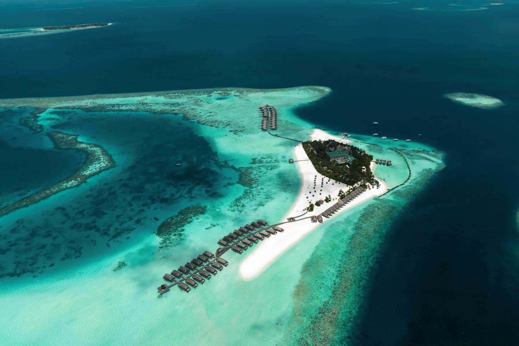 Veduta aerea del Constance Moofushi con bungalow sull'acqua e spiaggia bianca.