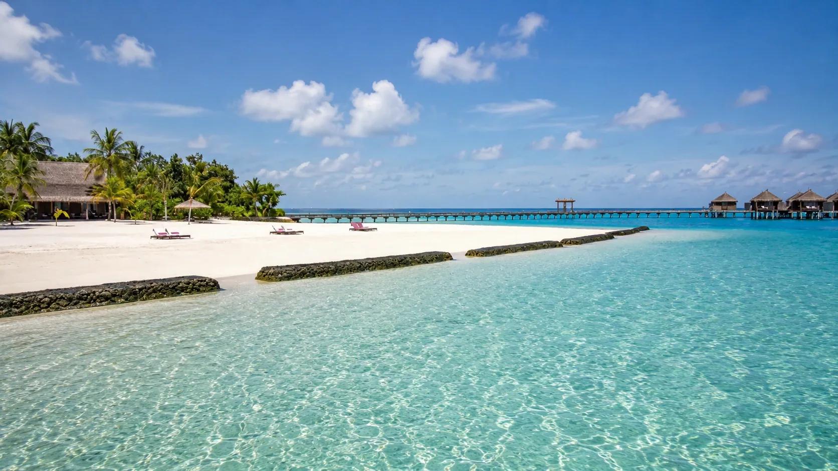 Spiaggia con lettini e palme al Constance Moofushi, acqua cristallina e pontile in legno.