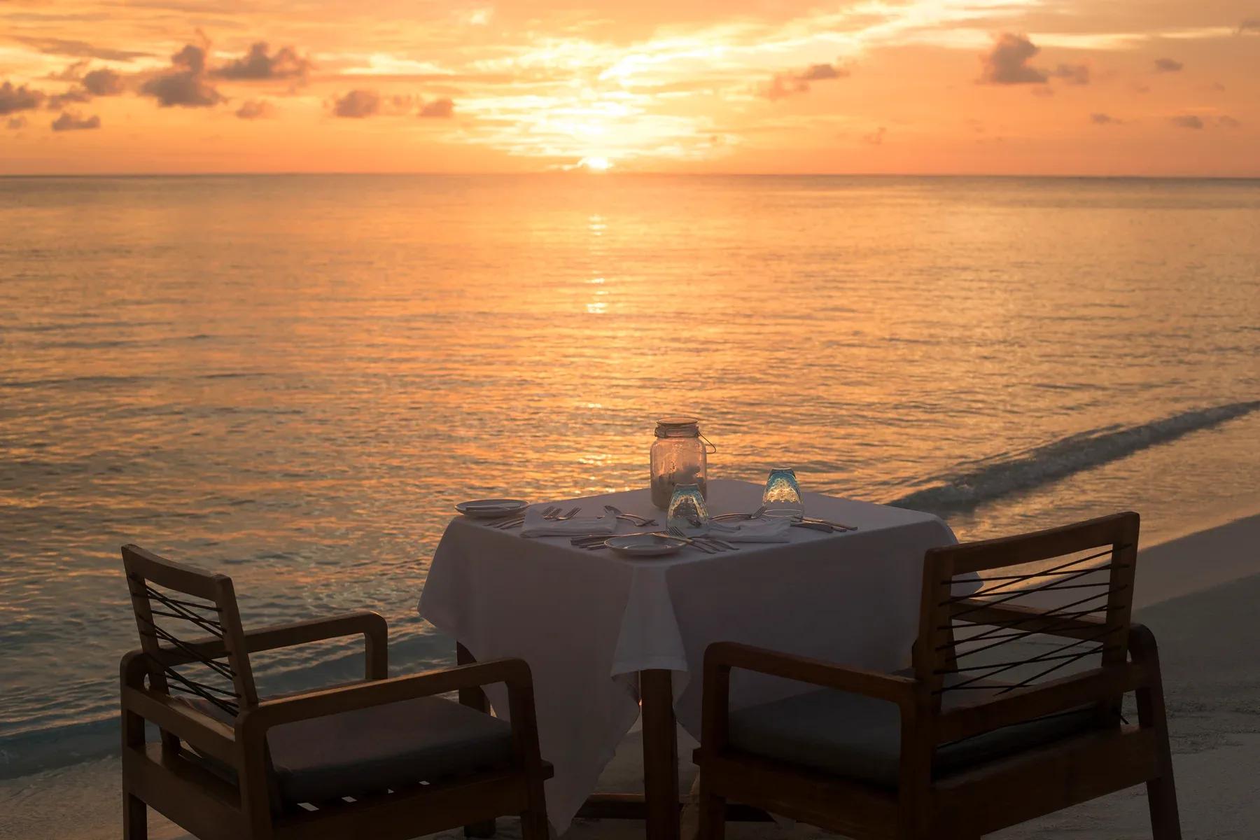 Cena sulla spiaggia con tavolo apparecchiato al tramonto al Constance Moofushi.