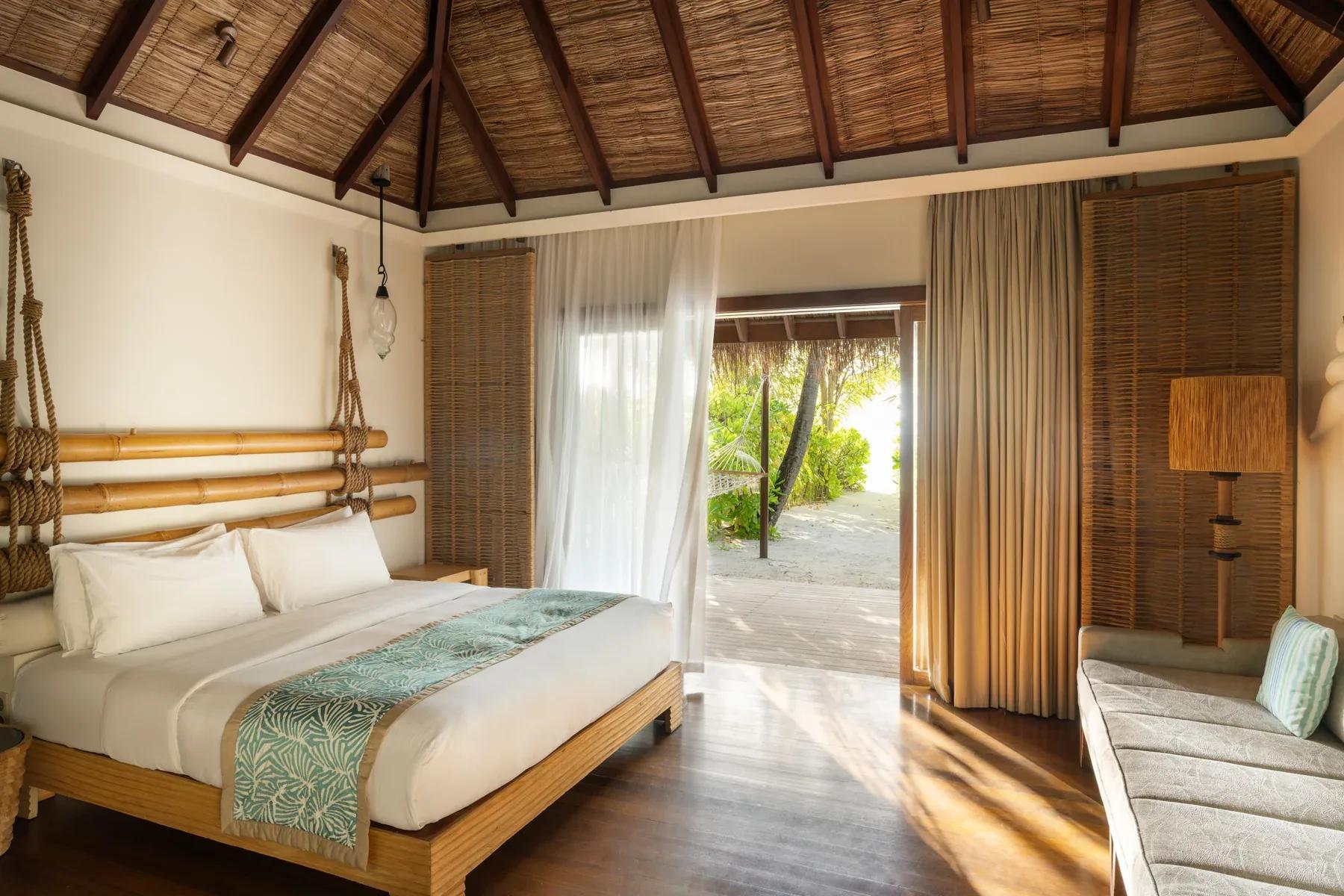 Interno delle Beach Villas con letto matrimoniale e vista sul terrazzo privato al Constance Moofushi.