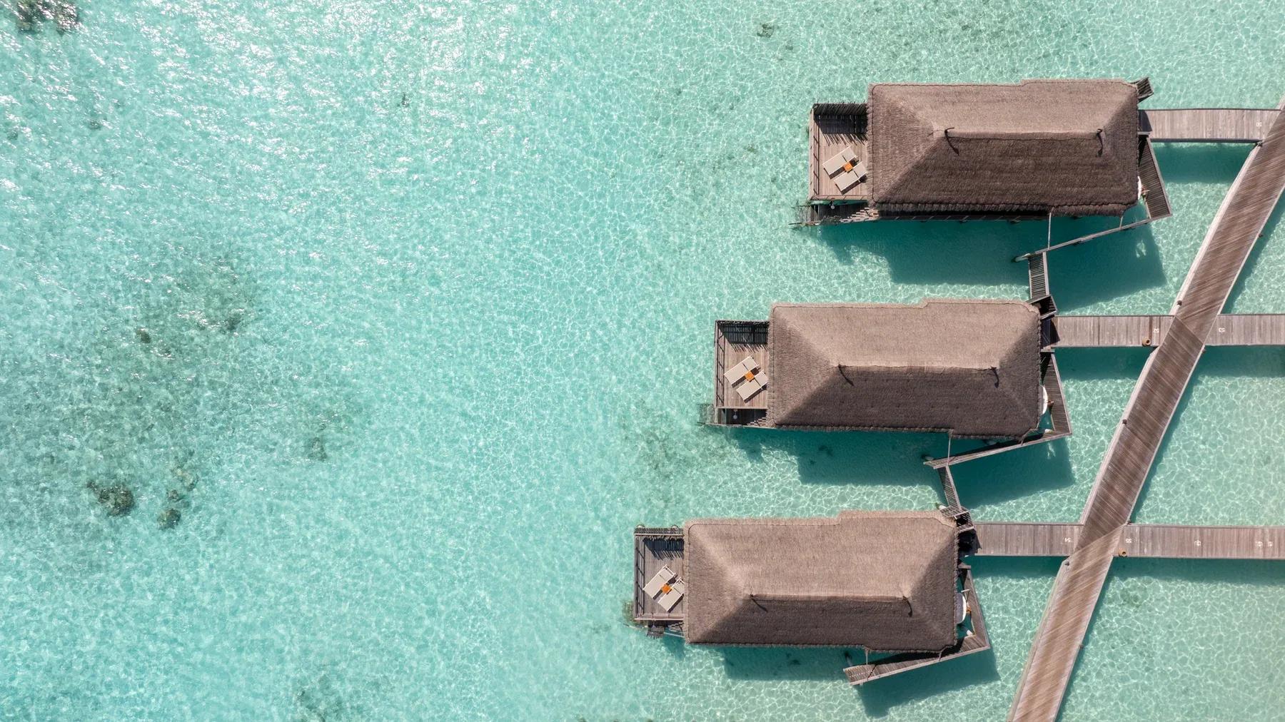 Vista aerea delle Water Villas con tetti in paglia e terrazze private sul mare del Constance Moofushi.