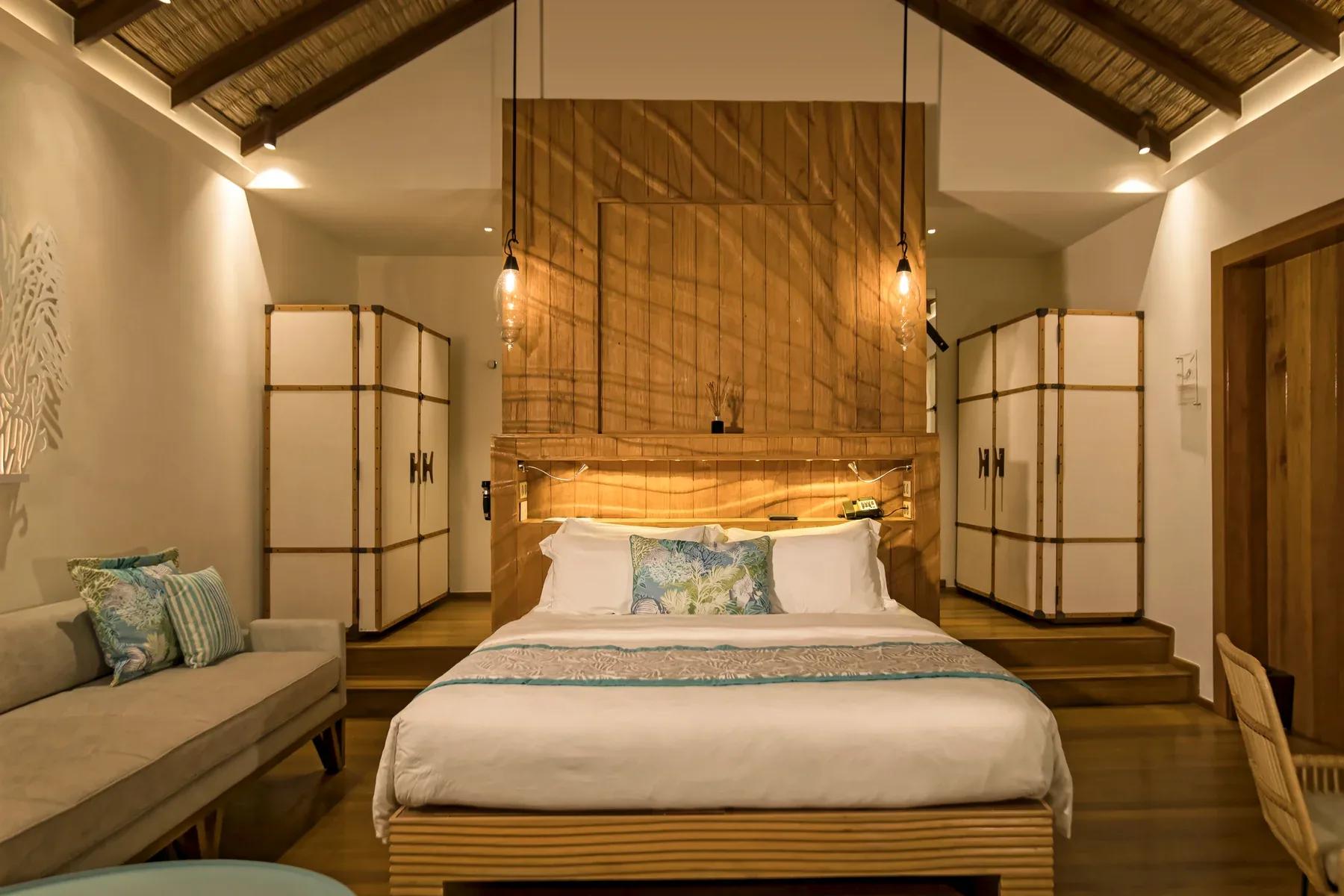 Interno delle Water Villas con letto matrimoniale, divano e illuminazione soffusa al Constance Moofushi.