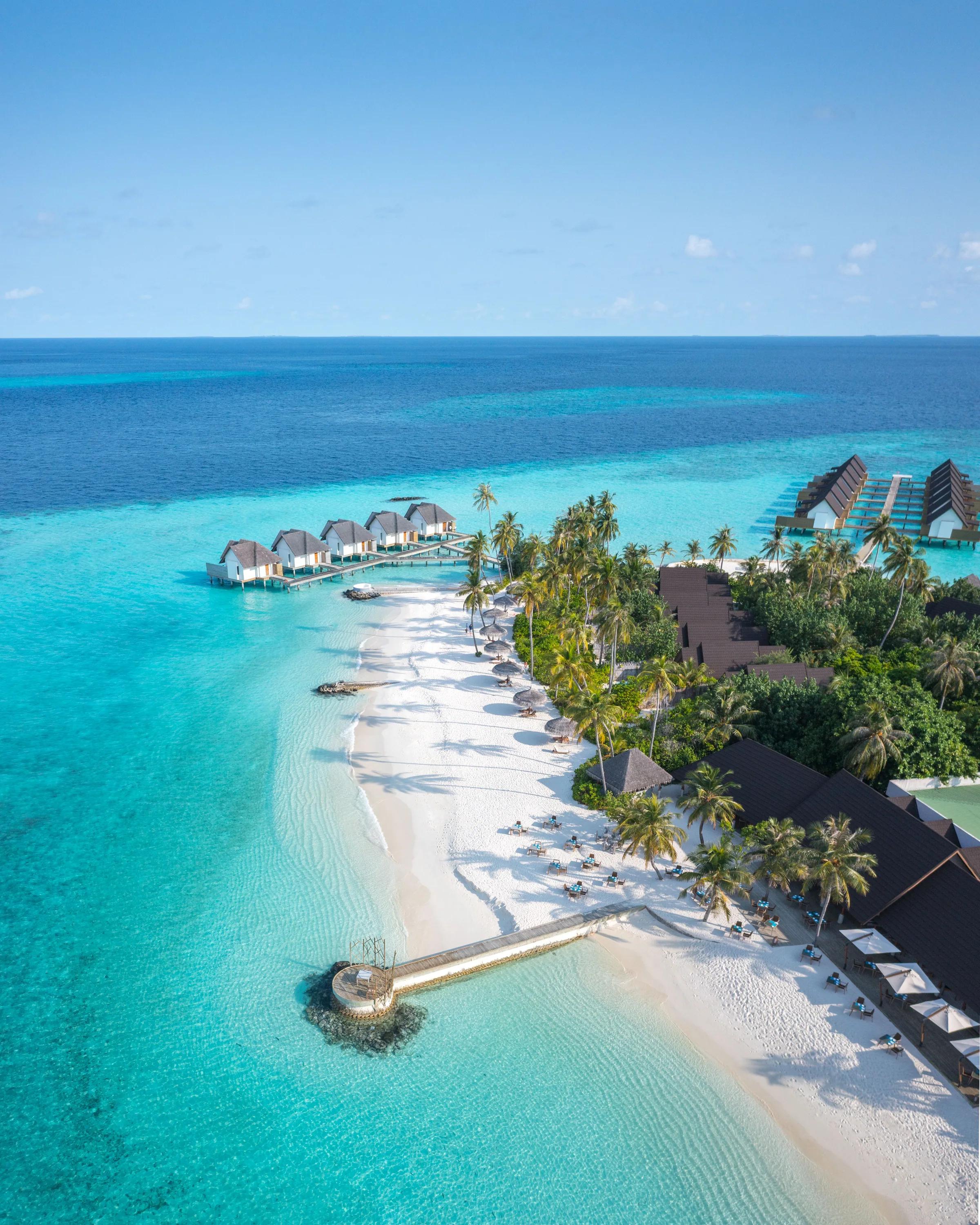 Vista aerea della spiaggia bianca e delle ville sull'acqua al Fushifaru Maldives con acque turchesi.