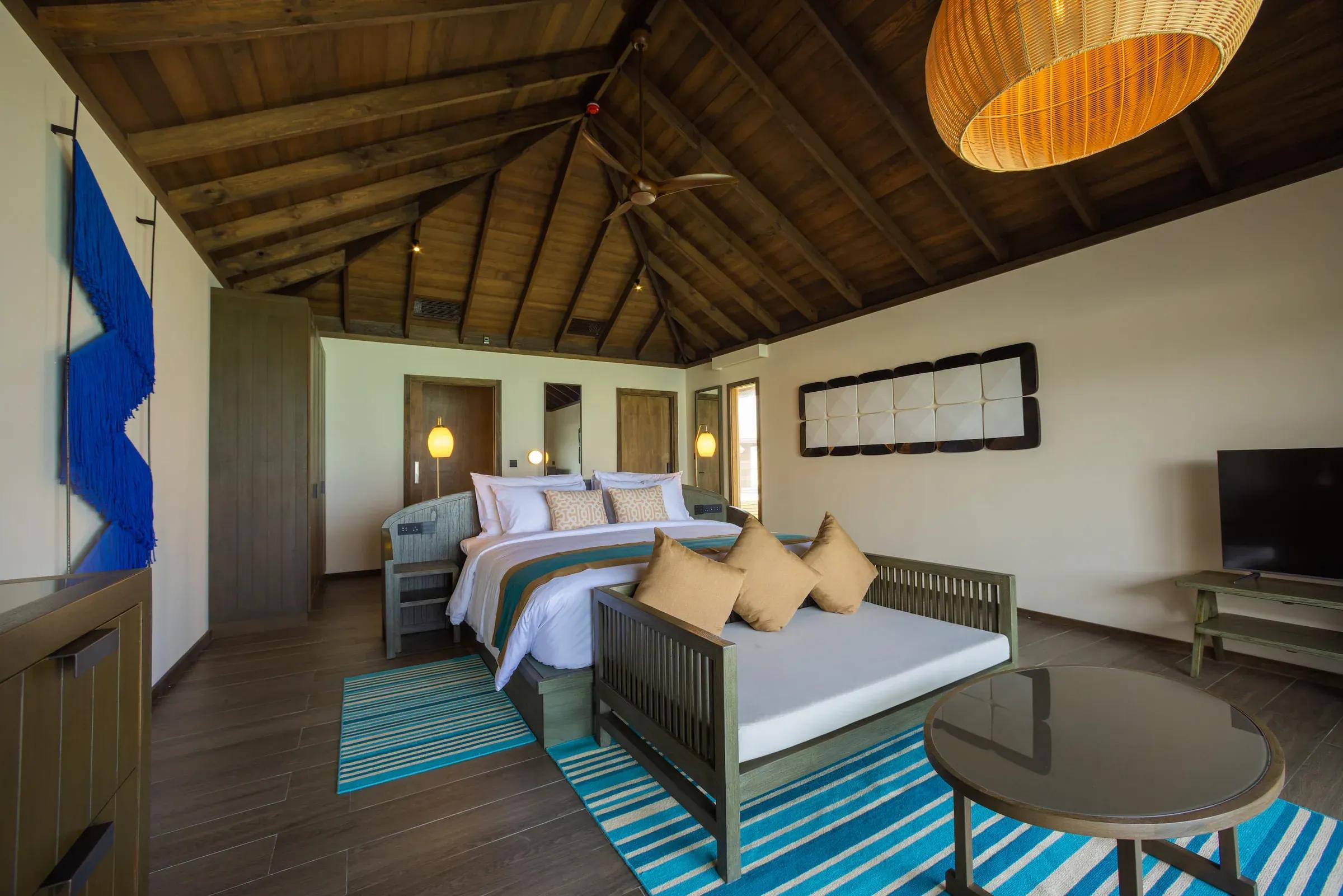 Interno della Dheru Water Pool Villa con soffitto in legno, letto matrimoniale e divano. Jawakara Islands Maldives.
