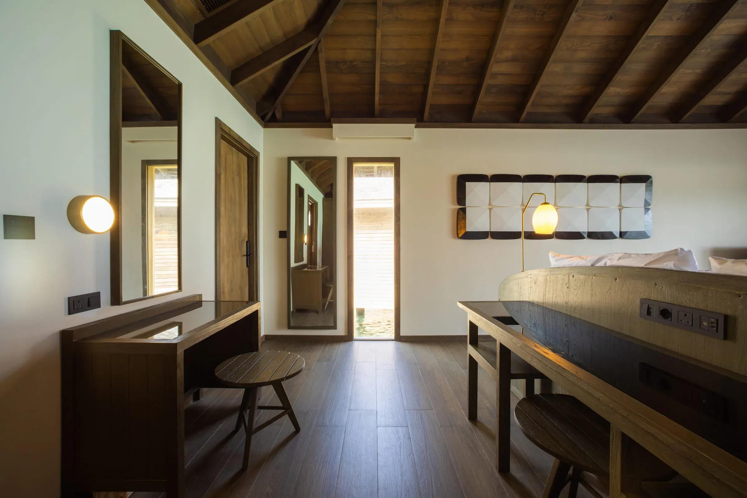 Camera con letto, scrivania e soffitto con travi in legno nella Dheru Water Pool Villa al Jawakara Islands Maldives