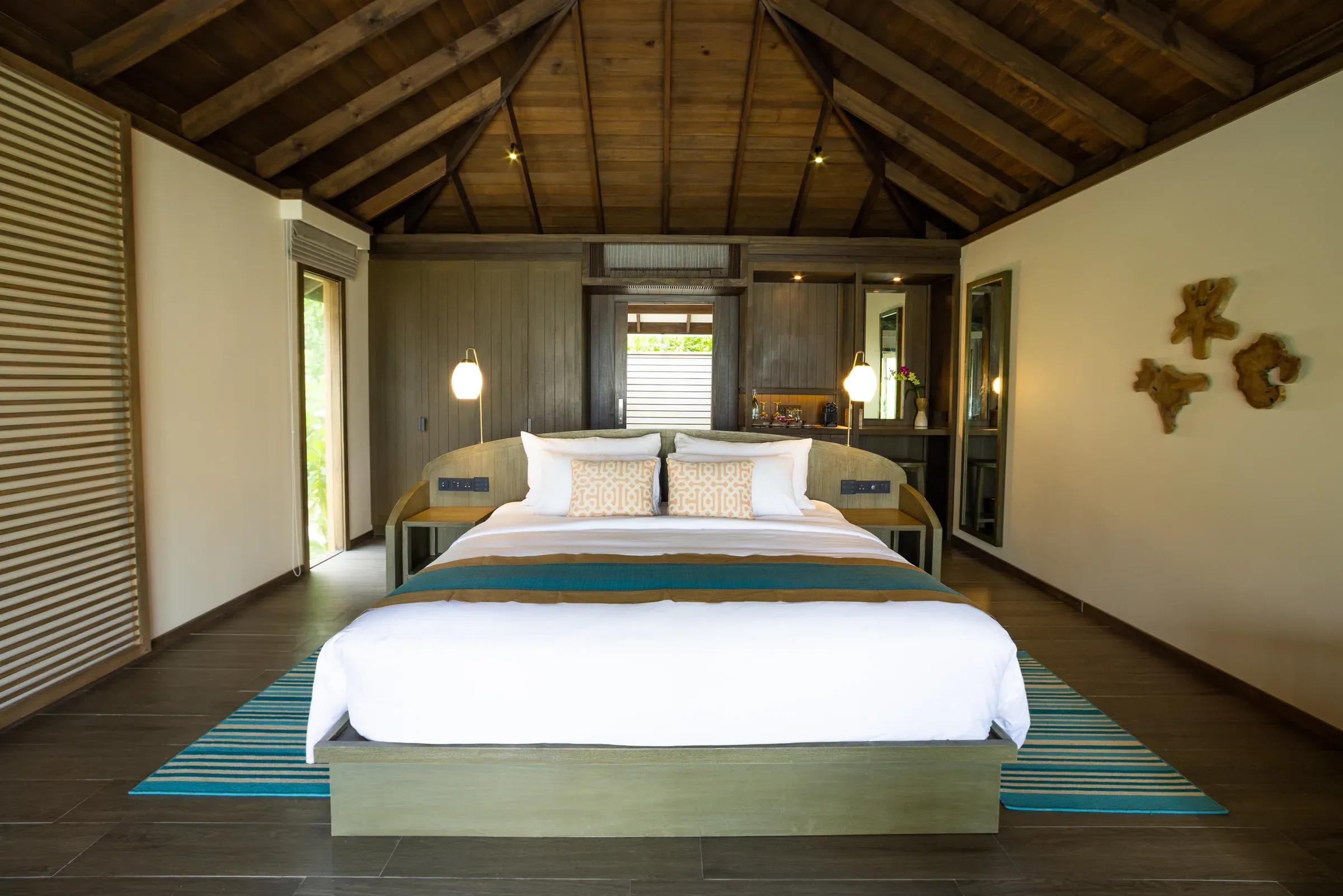 Interno della Mabin Beach Pool Villa con letto matrimoniale e arredamento in legno al Jawakara Islands Maldives.