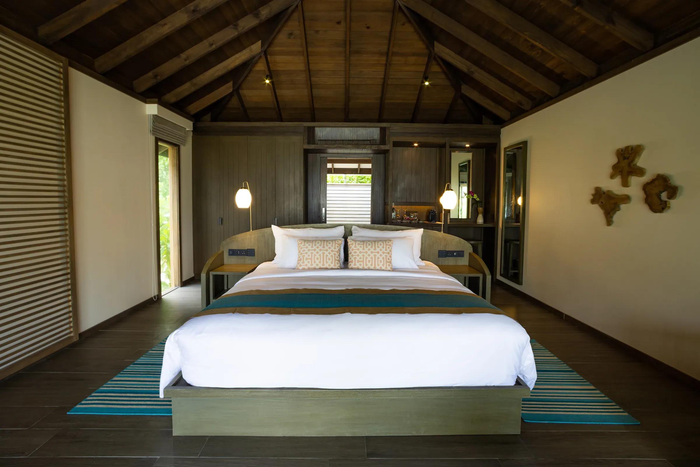 Camera della Mabin Beach Villa con letto matrimoniale e soffitto in legno al Jawakara Islands Maldives.