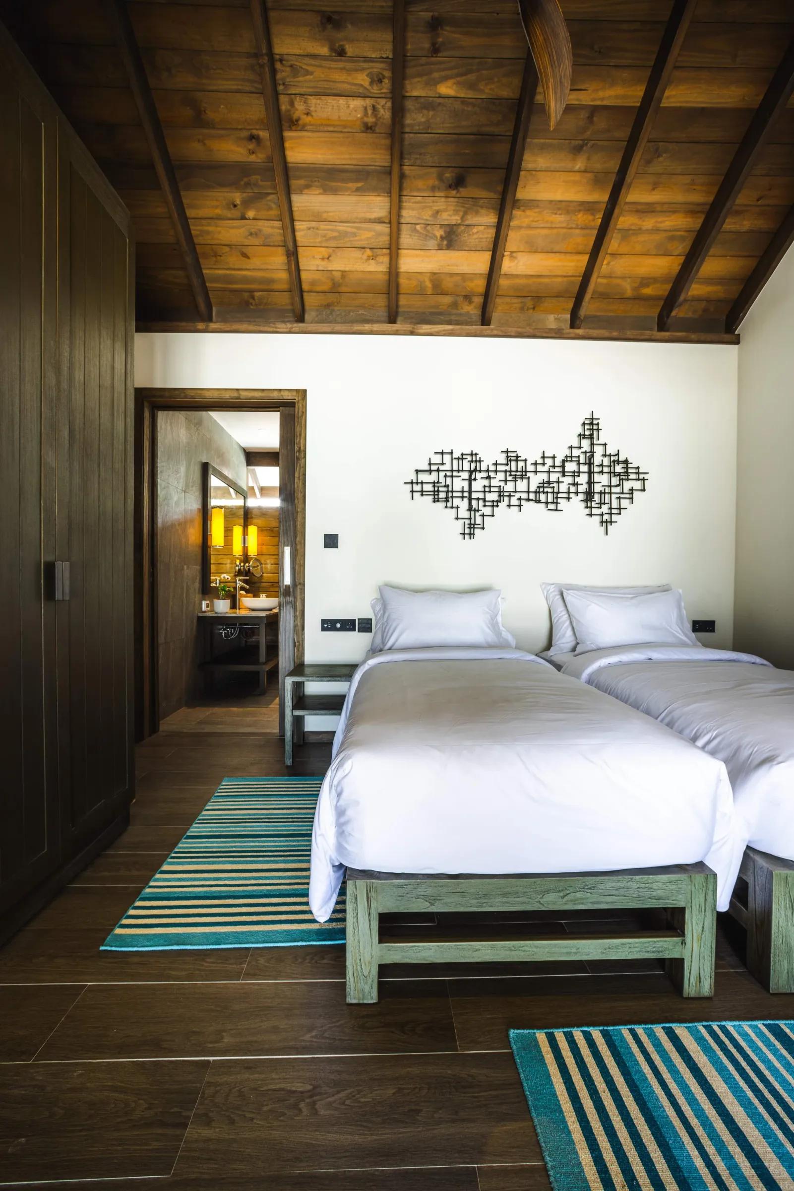 Camera della Mabin Three Bedroom Villa con letti singoli, soffitto in legno e decorazione murale al Jawakara Islands Maldives.