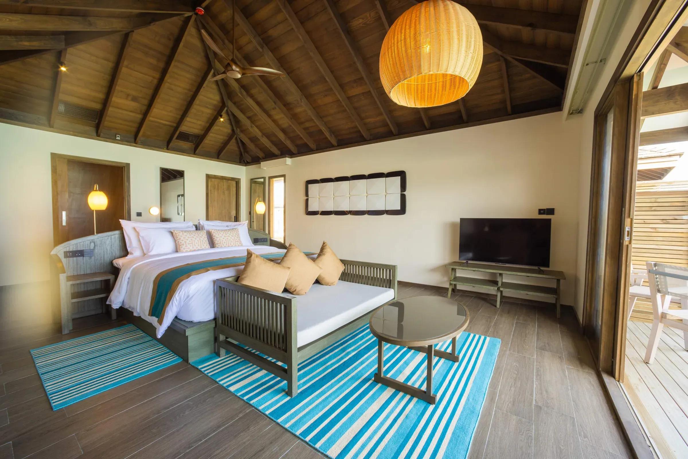 Interno della Mabin Water Pool Villa con letto matrimoniale, divano e lampadario a sospensione presso Jawakara Islands Maldives.