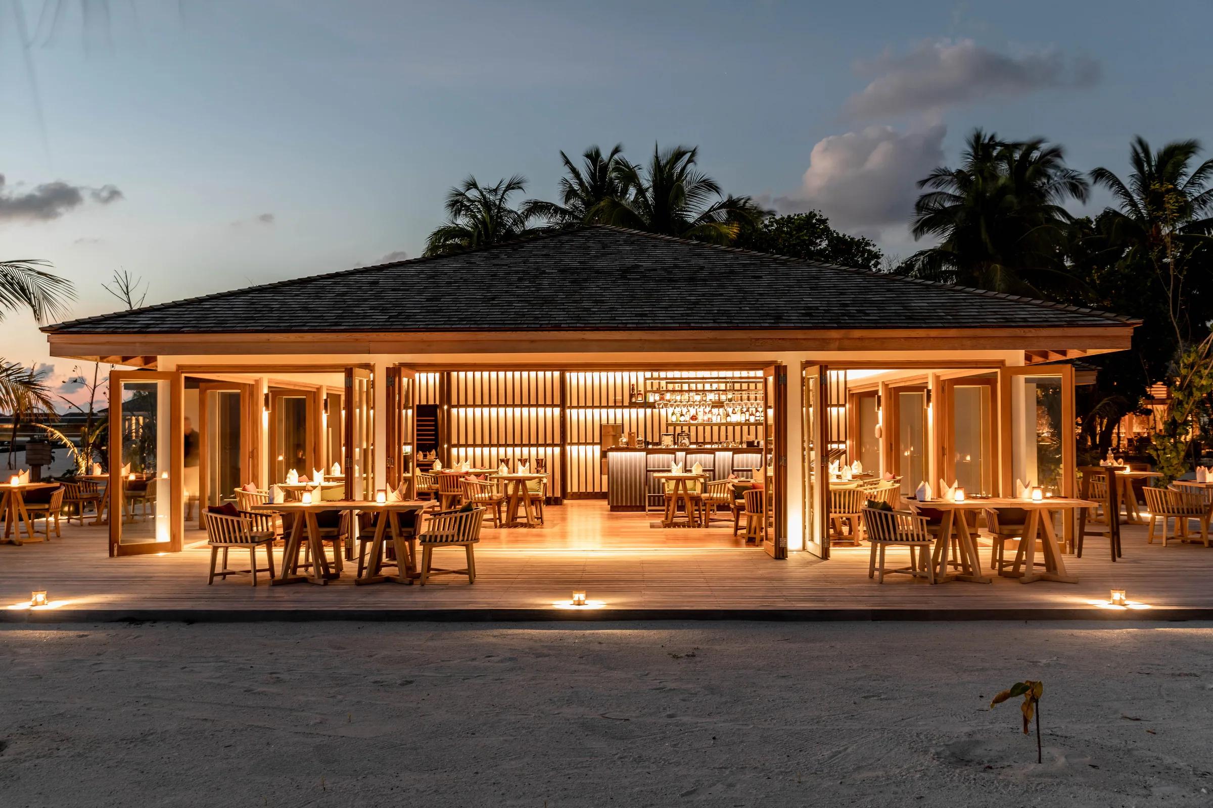Ristorante all'aperto illuminato davanti al Kagi Maldives Spa Island con tavoli e sedie.