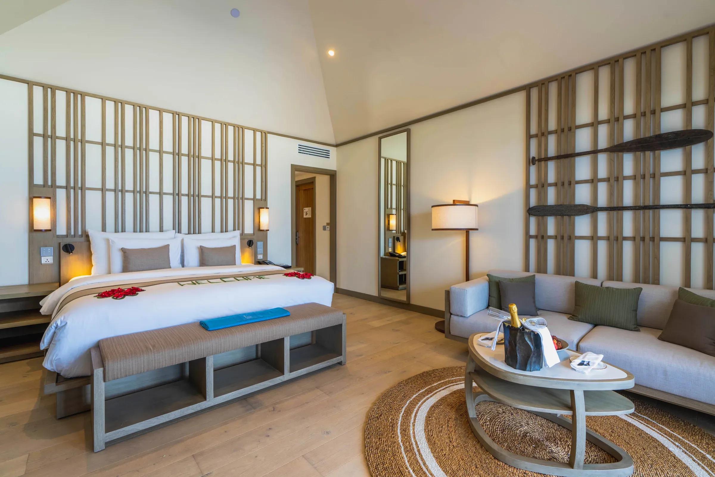 Interno della Beach Pool Villa con letto matrimoniale e area salotto al Kagi Maldives Spa Island.
