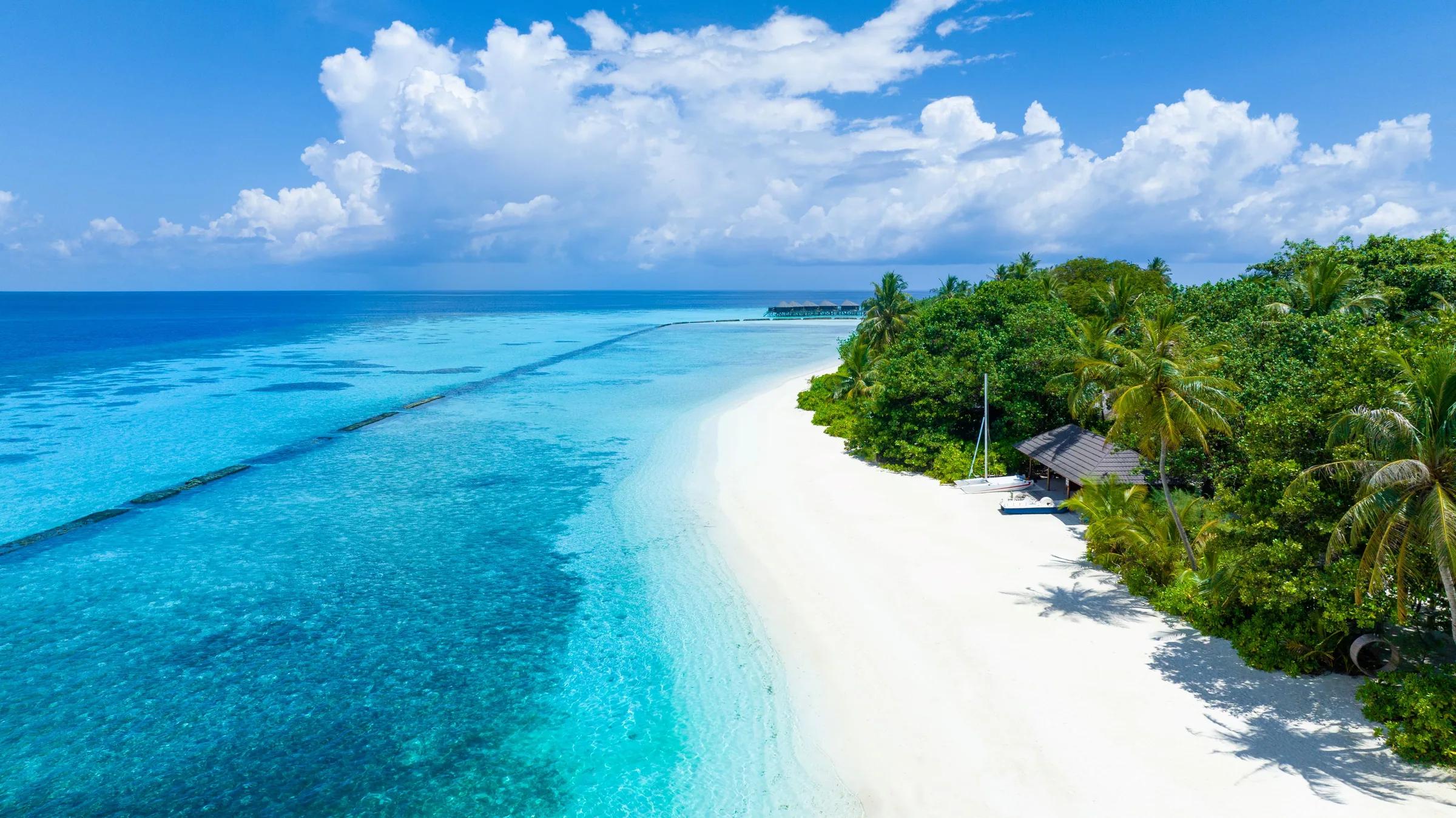 Spiaggia di sabbia bianca e laguna turchese con palme tropicali al Komandoo Island Resort & Spa alle Maldive.