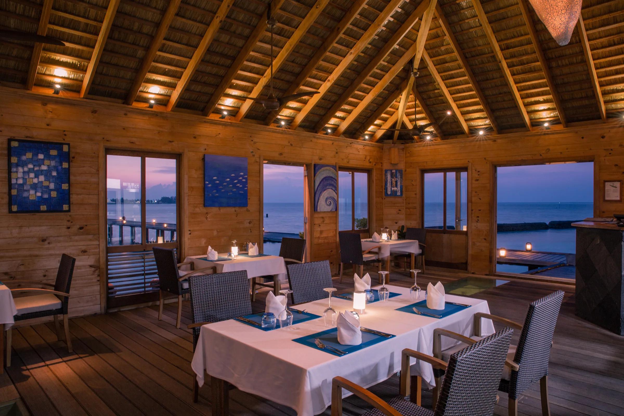 Aqua restaurant con tavoli apparecchiati e vista mare al tramonto al Komandoo Island Resort & Spa