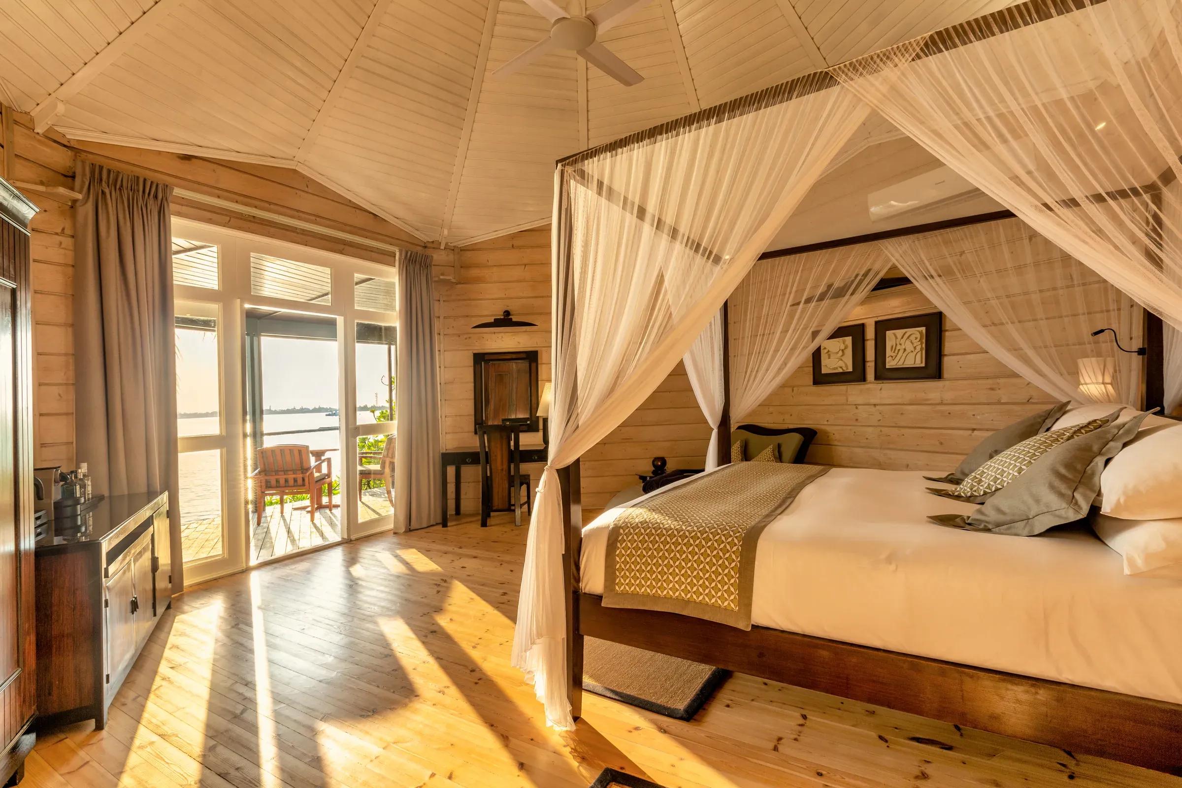 Interno della Premium Jacuzzi Beach Villa con letto a baldacchino e vista sulla terrazza del Komandoo Island Resort & Spa.