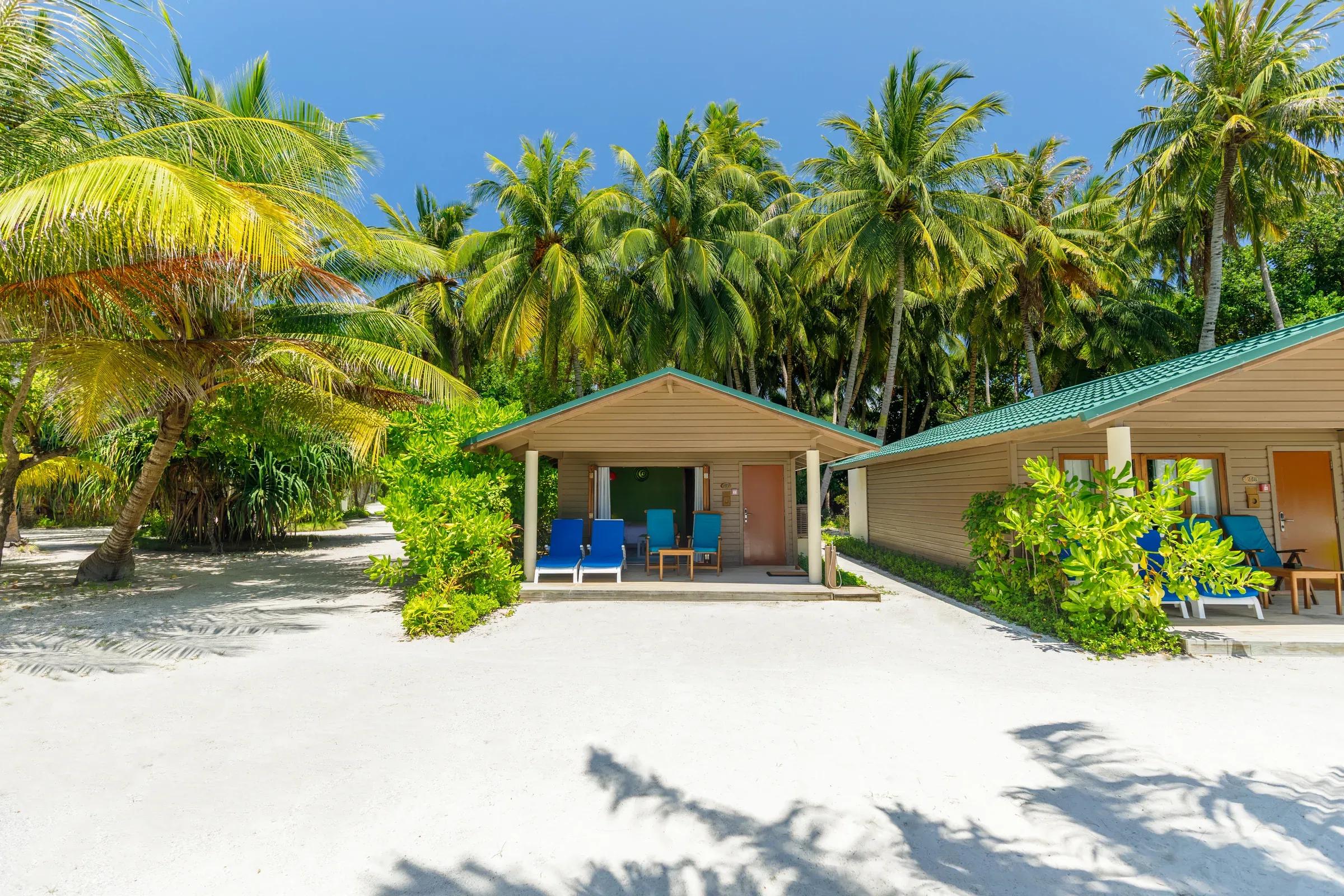 Beach Villa con terrazza e lettini blu sulla spiaggia bianca circondata da palme al Meeru Island Resort & Spa