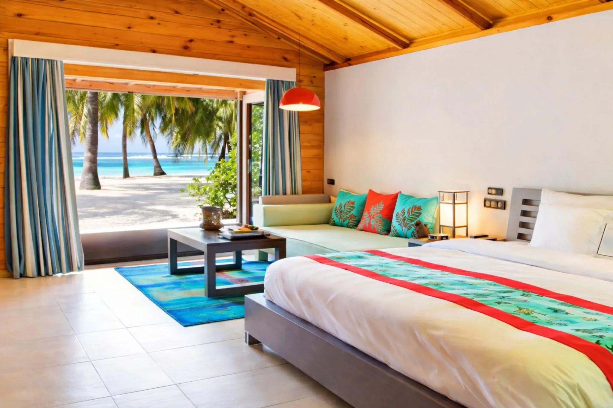 Camera Beach Villa con letto, divano e vista su spiaggia con palme al Meeru Island Resort & Spa