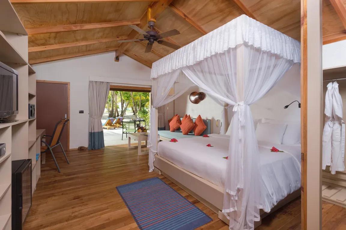 Interno della Jacuzzi Beach Villa con letto a baldacchino e accesso alla terrazza del Meeru Island Resort & Spa.