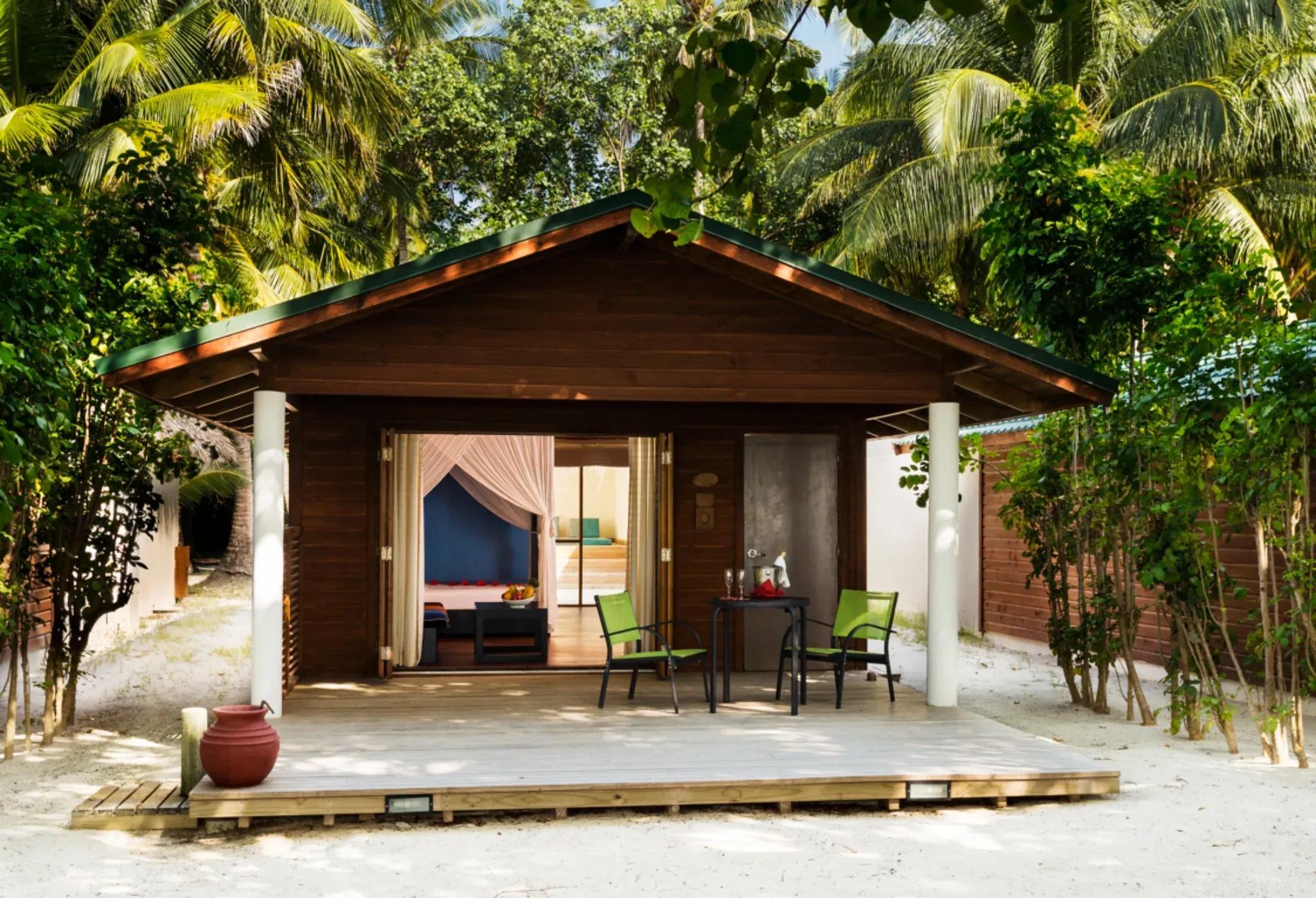 Veranda della Jacuzzi Beach Villa con sedie e tavolo, circondata da vegetazione al Meeru Island Resort & Spa.