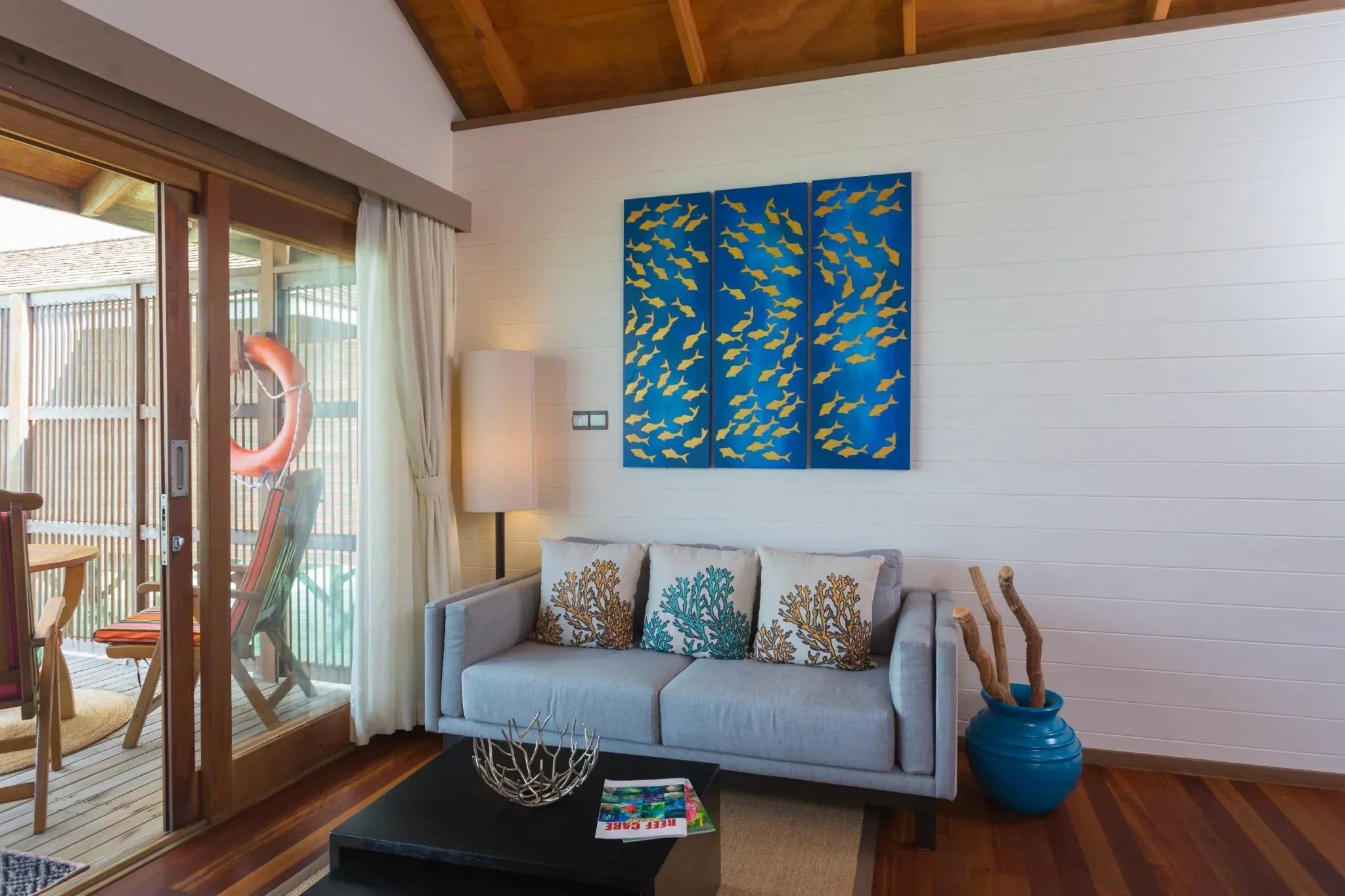 Interno della Jacuzzi Water Villa con divano grigio e arte murale al Meeru Island Resort & Spa.