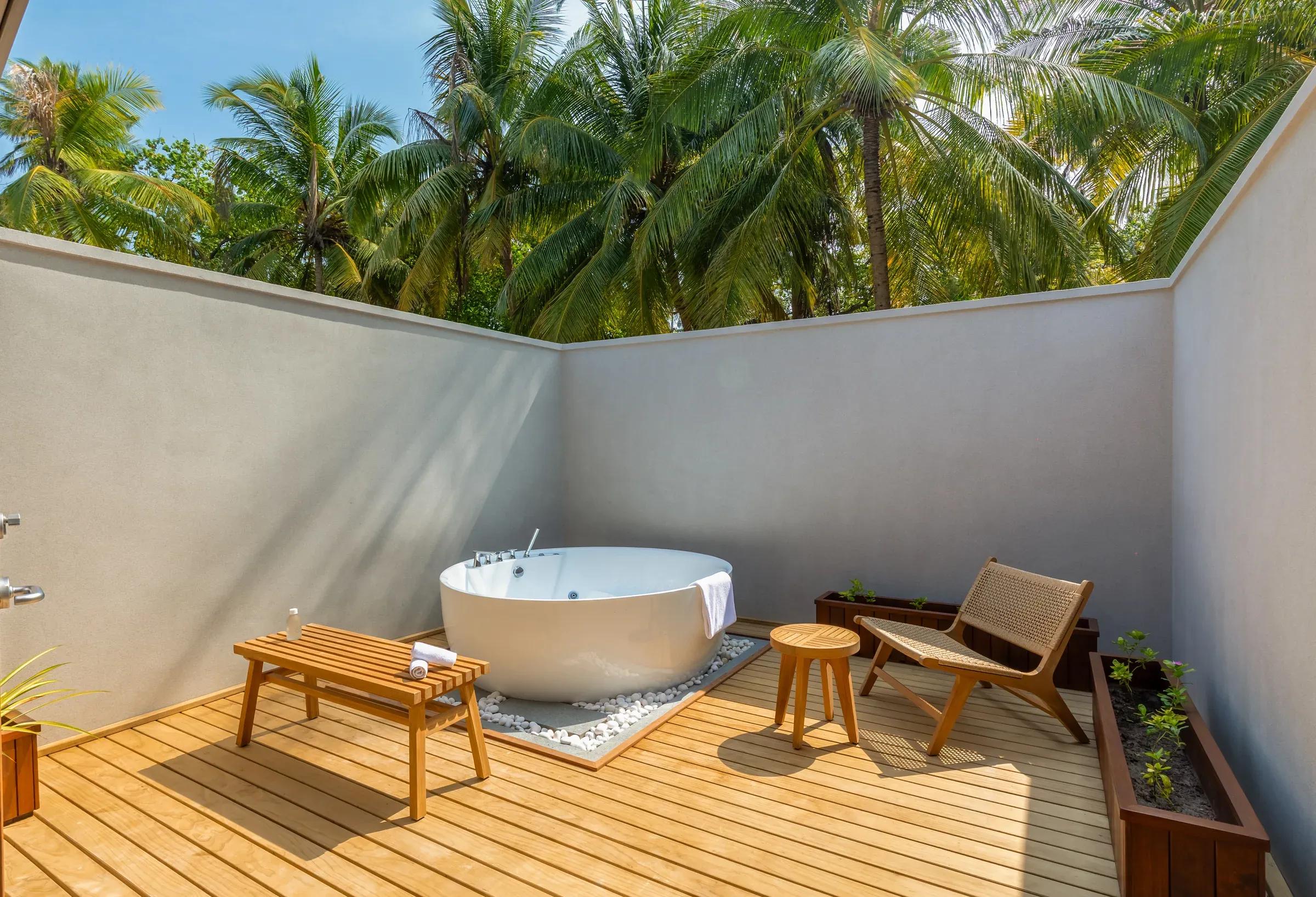 Area esterna della Two Bedroom Beach Pool Villa con vasca e sedute in legno al Meeru Island Resort & Spa.