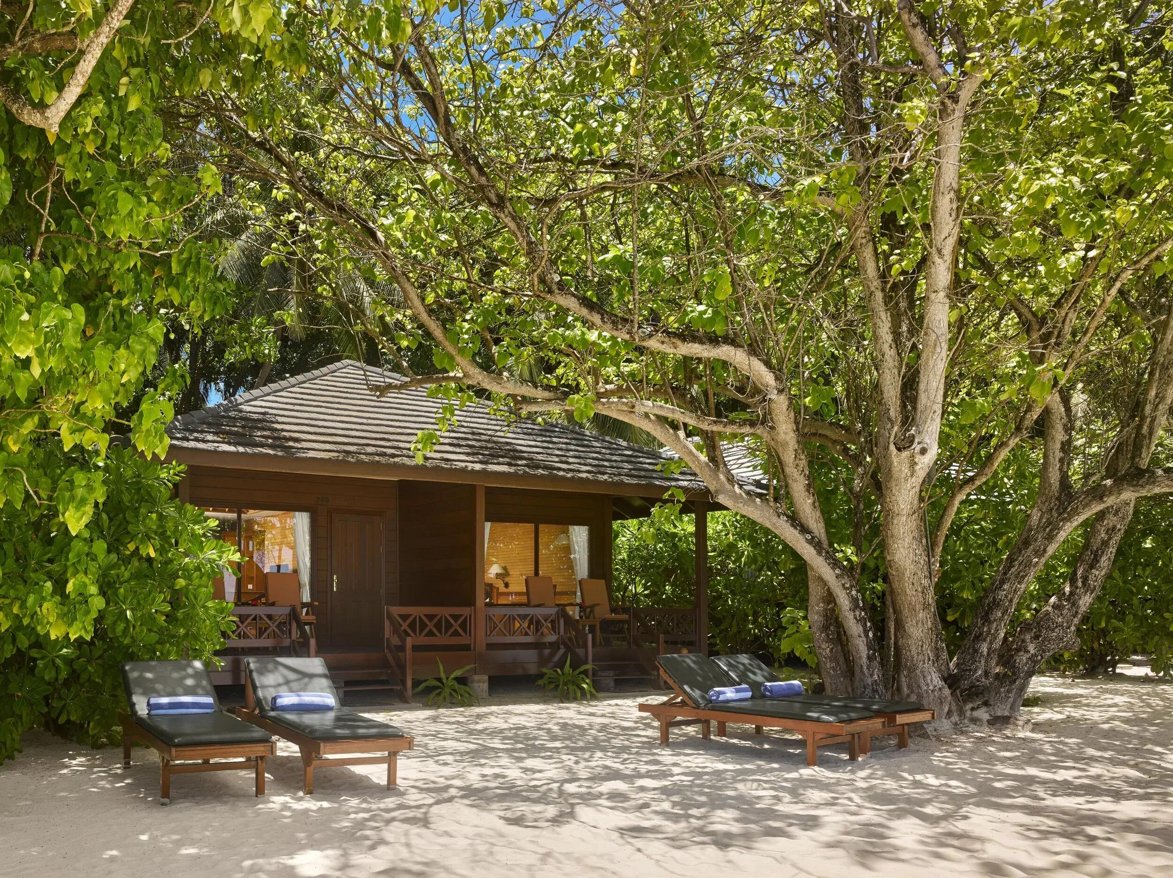 Beach Villa con sedie in legno, lettini e alberi sulla sabbia, Royal Island Resort & Spa.