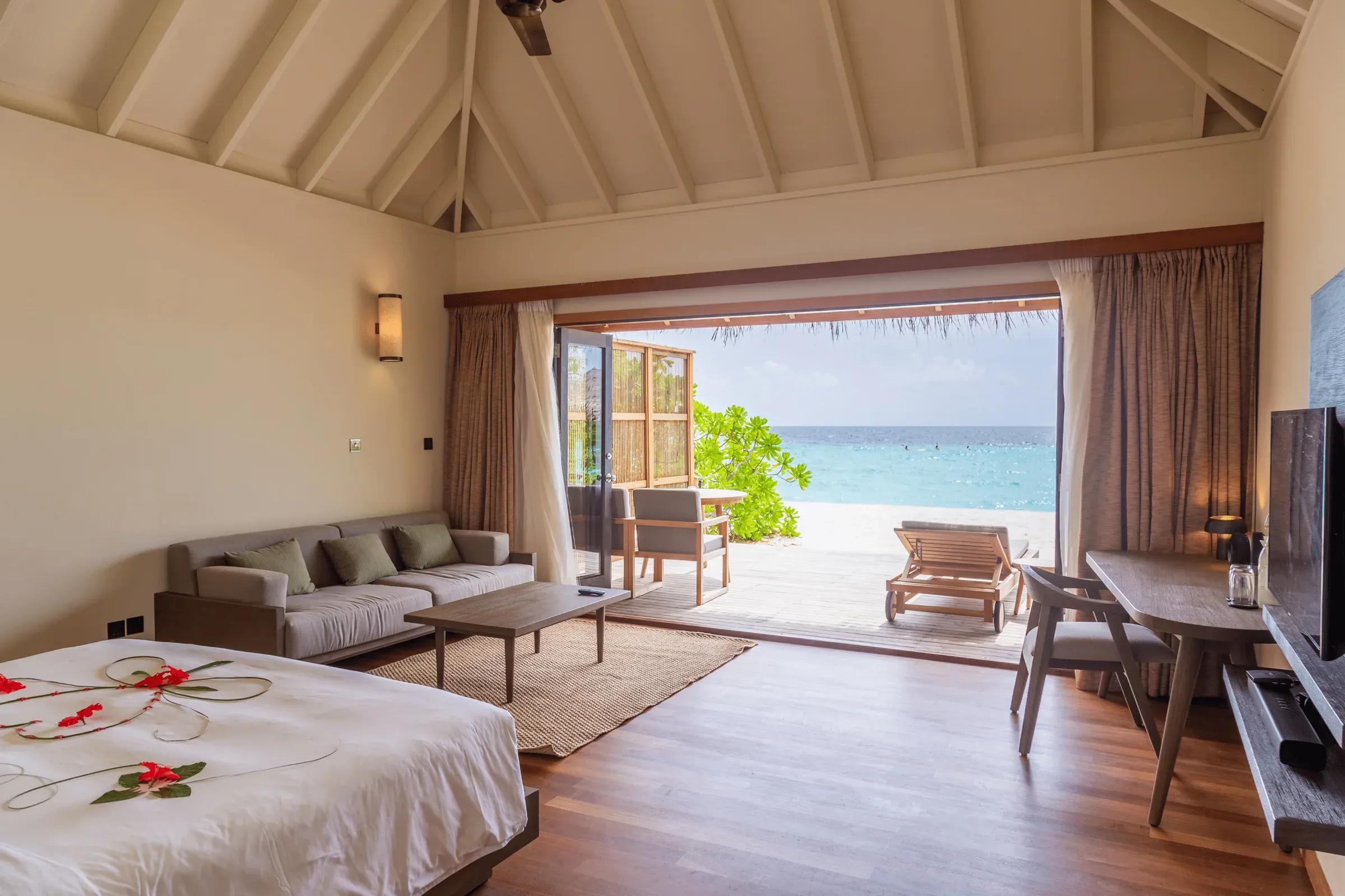 Vista interna della Jacuzzi Beach Villa con letto, divano e terrazza con lettino al Veligandu Island Resort & Spa.