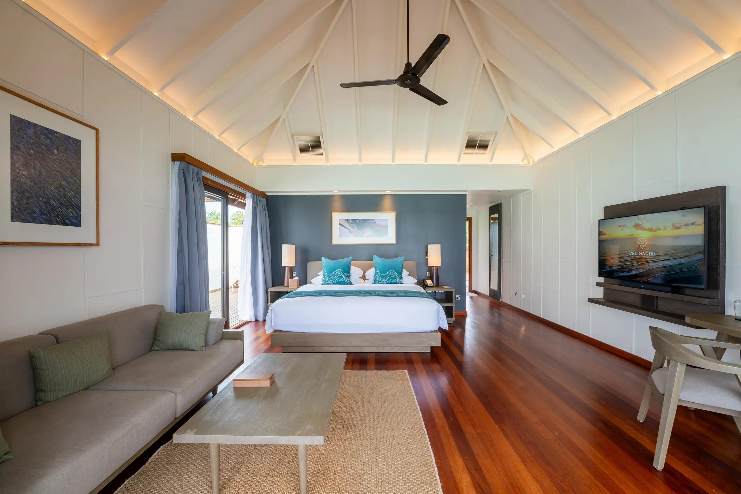 Camera da letto e divano della Sunset Ocean Villa al Veligandu Island Resort & Spa con soffitto a volta e pavimento in legno.